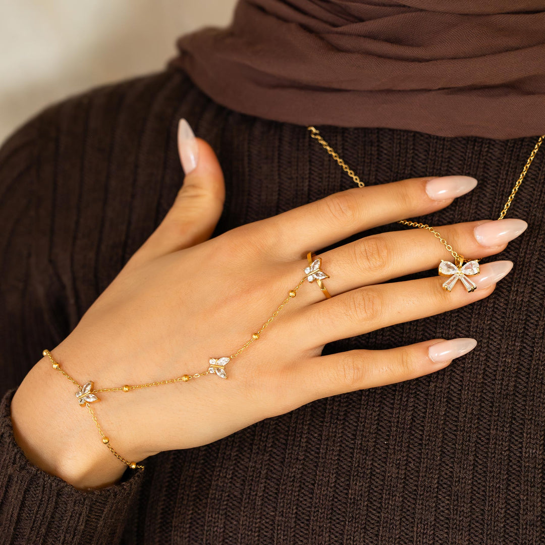 Hand wearing gold butterfly-themed jewelry with a brown background