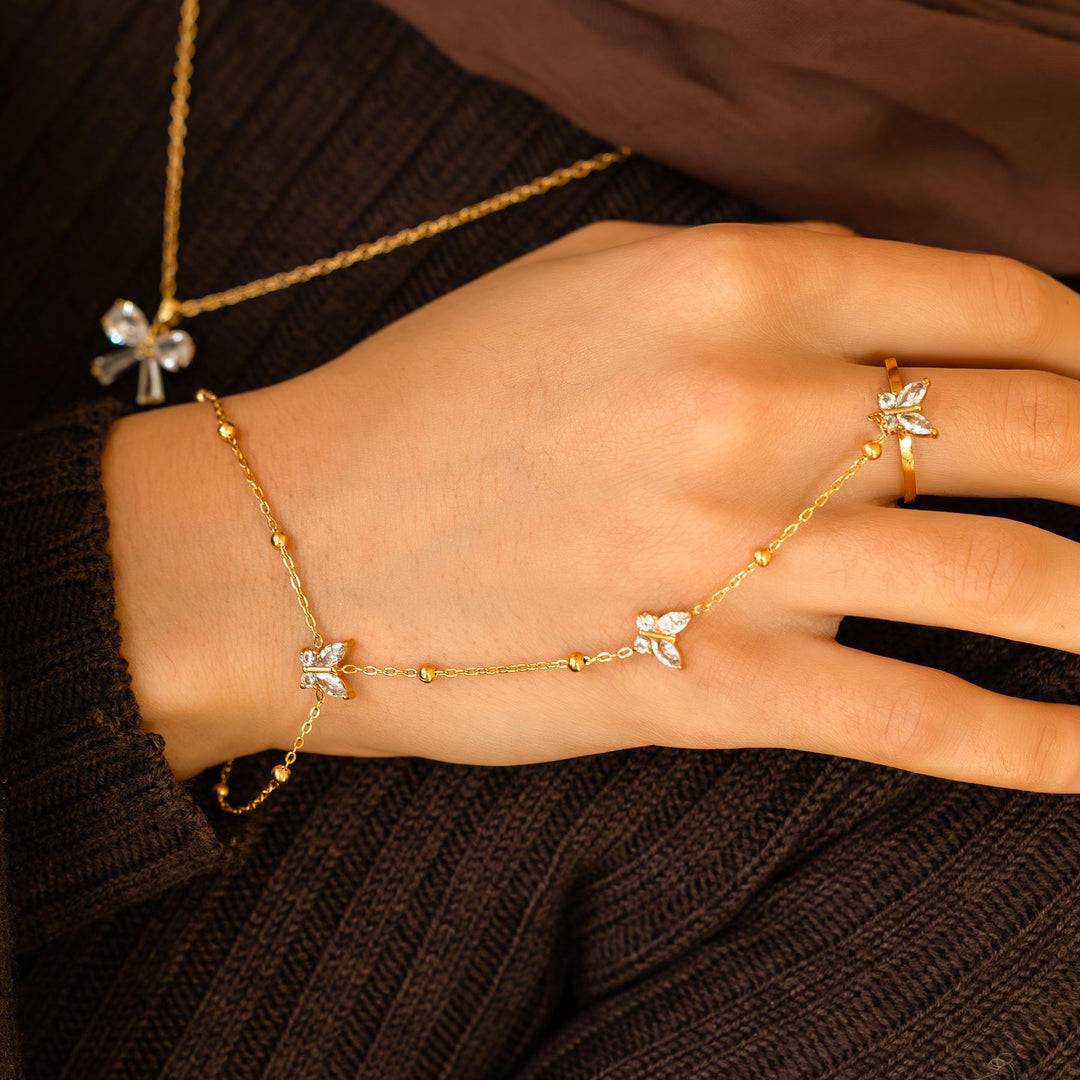 Gold bracelet and ring with butterfly designs on a hand against a brown background