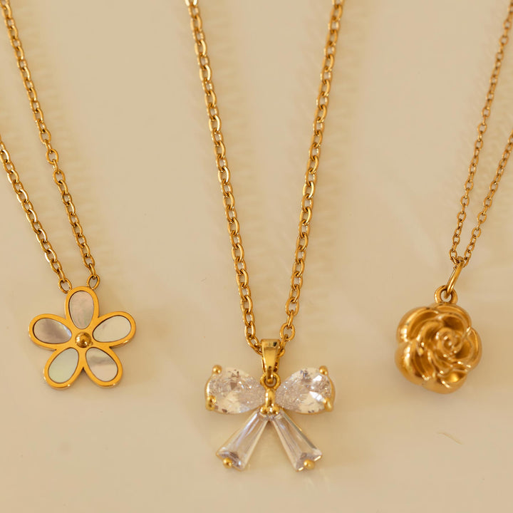 Three gold necklaces with floral and bow pendants on a beige background
