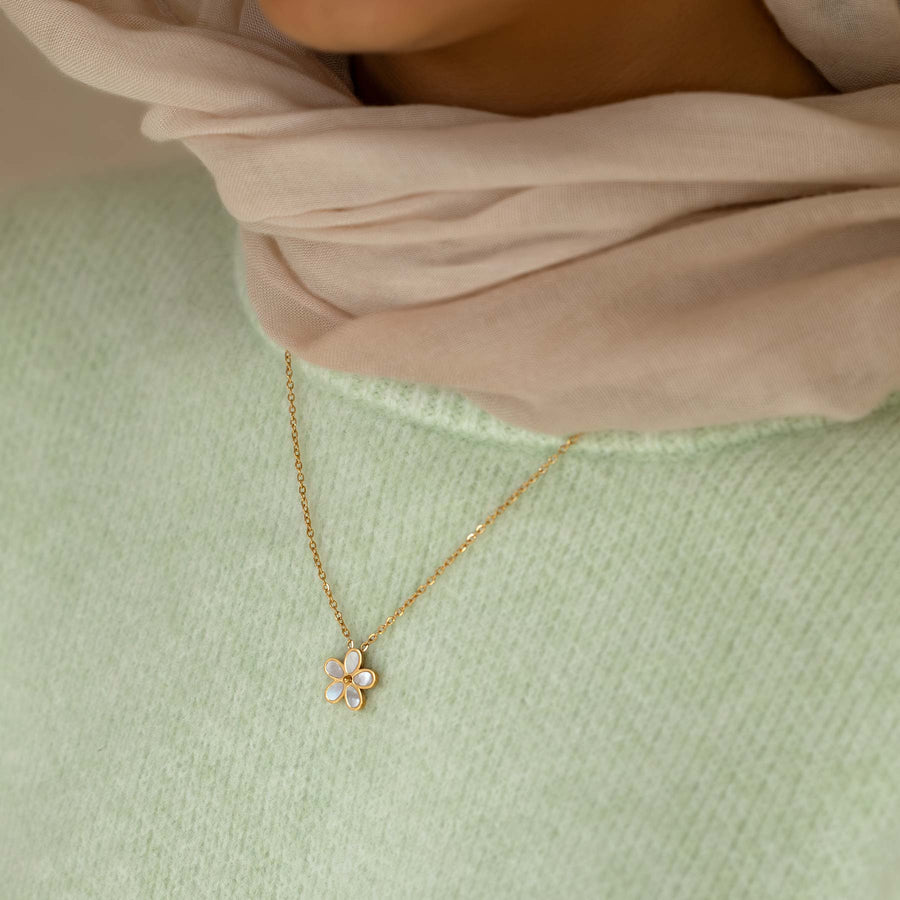 Gold necklace with a flower pendant worn by a person on a light green background