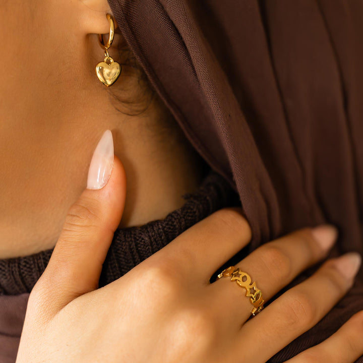 Close-up of a person wearing gold heart earrings and a gold ring with a brown garment.